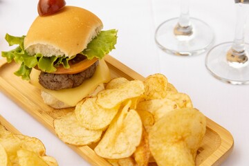 Top closeup of a burger and chips on the wooden plate on the white background