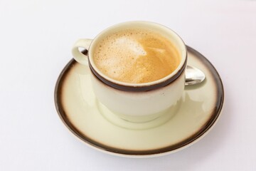 Top closeup of a cup of cappuccino on a plate with brown edges and a little spoon near