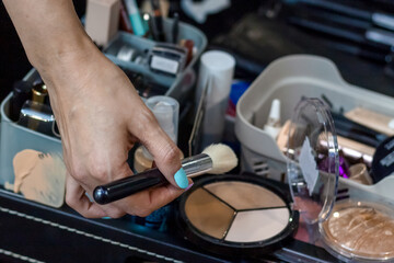 The makeup master is getting ready for work. The makeup artist's hand picks up a multi-colored...