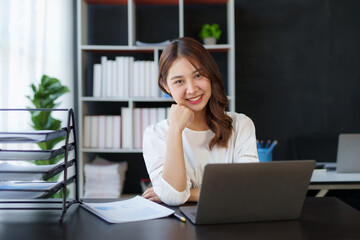 Attractive young Asian businesswoman using laptop in office smiling and looking at camera.