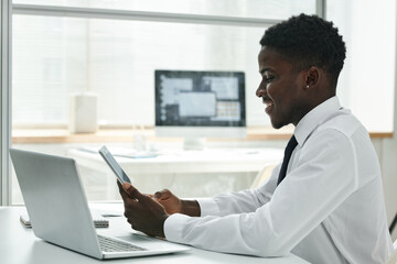 Young African American businessman using wireless devices at his workplace at office, he working online on digital tablet
