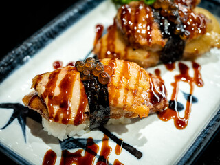 Two foie gras sushi with sauce served on white plate on dark table, japanese food style. Burnt foie...