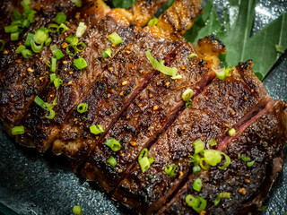 Close-up Australian sliced medium rare wagyu grilled beef steak top with sliced spring onion on glass plate on dark background, japanese style. Australian grilled meat texture.