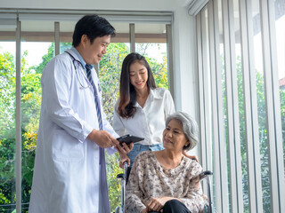 Obraz premium Happy senior woman patients in wheelchair with grandchild take her to meet doctor male use tablet discussing her medical treatment records in hospital. Senior adult checkup appointment concept.