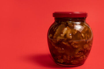 Jar of walnuts in honey on red background