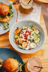 Vertical closeup shot of a gourmet pomegranate salad and a juicy burger on a restaurant table