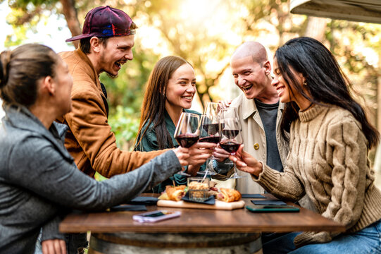 Group of smiling friends drinking and toasting red wine in the garden of restaurant bar - Friendship concept with happy young people having fun together during happy hour.