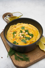 Hummus with spices, herbs, olive oil on wooden on a gray background.