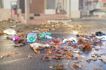 Plastic garbage scattered on the asphalt in the city among the autumn leaves. Environmental...