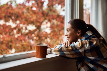 Young happy woman enjoying the view from her apartment window.