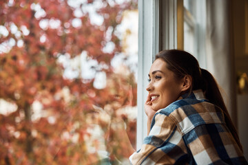 Pensive woman day dreaming while enjoying the view from her apartment window.