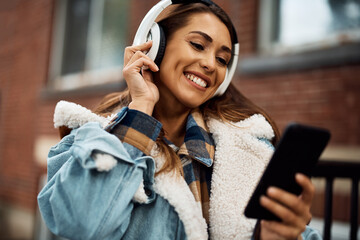 Young woman enjoys in music over headphones in the city.
