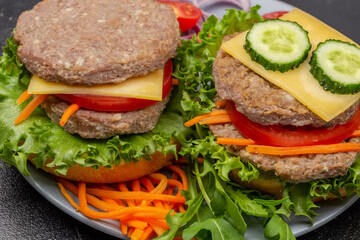 Two cheeseburgers with greens, chopped onion and carrots on gray plate.