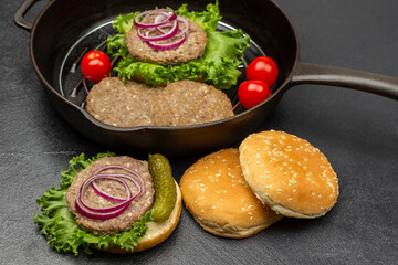 Grilled burger, pickle, onion and lettuce on round bun. Buns on the table