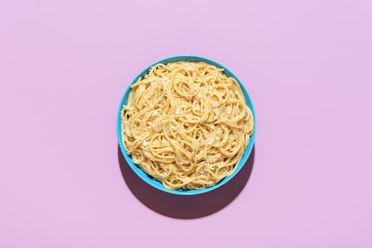 Spaghetti with cheese and black pepper, top view on a purple background