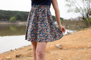 Woman in floral dress posing by lake. Her face is not seen in photo. 