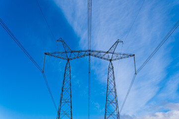 High voltage tower with electricity transmission power lines against blue sky, low angle view.
