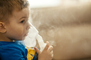 A little boy inhaling with nebulizer at home during his asthma attack. - obrazy, fototapety, plakaty