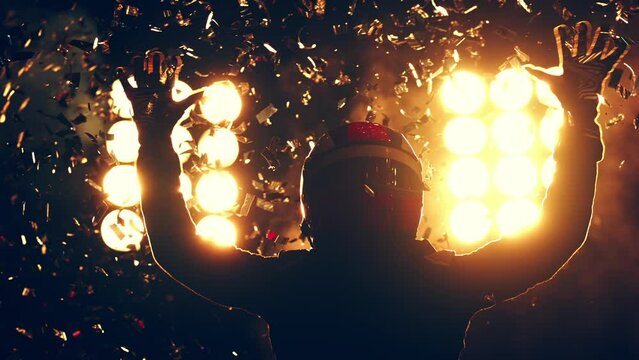 Silhouette of race car driver celebrating the win in a race against bright stadium lights. 100 FPS slow motion shot