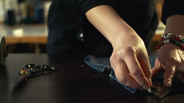 A female tailor seamstress marking hem on a pair of old vintage jeans in a workshop repairing old denim clothes. Small family business, tailoring and repair of clothes, handmade, startup. Close-up