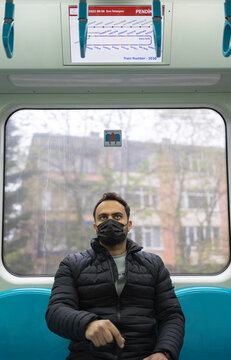 A passenger travelling with Turkish metro. He is in Pendik station ın Istanbul. He wears black medical mask. There is a board shows route behind him.