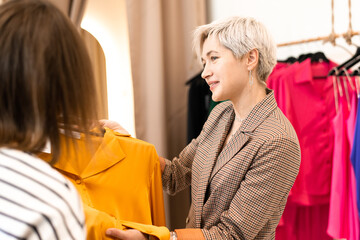 Young women choosing clothes at store, sales consultant offers wear