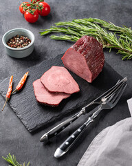 Juicy baked roast beef on a slate board with tomatoes, pepper and fresh herbs on a dark  background