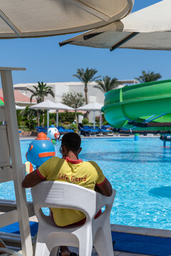 Ein Bademeister, life guard im gelben T-shirt am swimming pool, Rückenansicht.