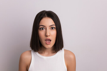 Fototapeta premium surprised beauty portrait of a beautiful cheerful young oriental woman in a white T-shirt in the studio on a white wall. make-up artist and hairdresser hairdresser in a beauty salon.