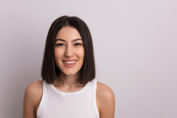 Fototapeta premium beauty portrait of a beautiful cheerful young oriental woman in a white T-shirt in the studio on a white wall. make-up artist and hairdresser hairdresser in a beauty salon.