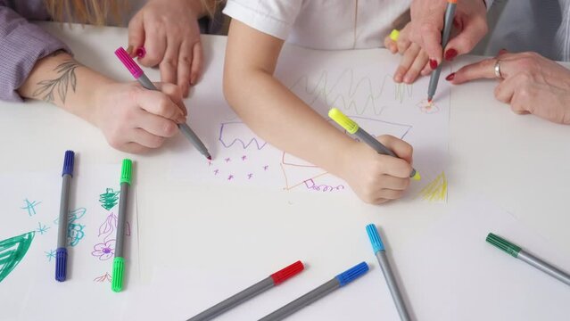 Family painting. Enjoying time. Creative art. Unrecognizable girl drawing with mother and grandmother together by colorful markers in light room interior.
