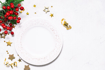 Festive Christmas and New Year table setting with empty white plate with ornament, fir tree branches and golden decorations on white marble surface. Festive menu template, copy space for your design.