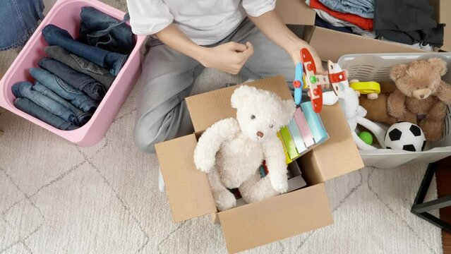 Boy preparing clothes and toys for charity donation. Teenage boy sorting and kid toys, clothes into boxes at home. Kid playing with old toys and packing them to cardboard box