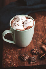 Hot chocolate drink with marshmallow in a cup on wooden board, dark background
