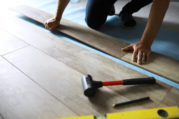 Installing laminated floor, detail on man hands blue wooden tile, over white foam base layer, small pile with more tiles background