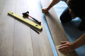 Installing laminated floor, detail on man hands blue wooden tile, over white foam base layer, small pile with more tiles background
