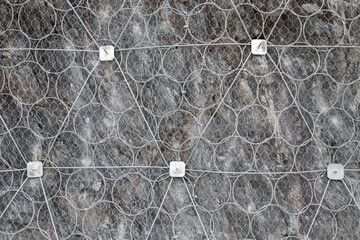 Gray rocky wall covered with protective metal wire
