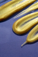 Creative cosmetic brushstrokes of gold paint isolated on a violet background. Gold paint texture. Yellow smears of cosmetics