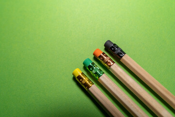 Wooden pencils with colorful erasers on green background 