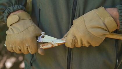 Close-up man hands in gloves cutting tree branch outdoors with knife. Tourist man hands in tactical...