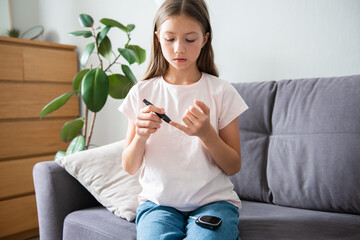 Teen diabetic girl measuring glucose sitting on the sofa at home. Health care and Medical,...