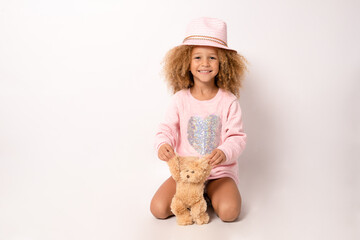 Little child girl wearing straw hat is hugging teddy bear isolated over white background.
