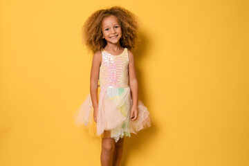 Happy child girl wearing a festive dress standing isolated over yellow background.