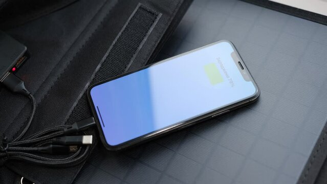Hands plug in portable solar panel charging iphone by mutlipurpose cable, power bank, watches, laptops, smartphone. Clean energy for using in camping or at home when NO electricity