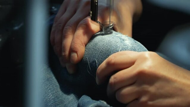 A female tailor seamstress repair old jeans with vintage darning machine in a workshop repairing denim clothes. Small family business, tailoring and repair of clothes, handmade, startup. Close-up