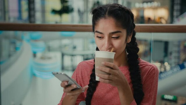 Arabian student freelancer woman girl lady sit at cafe table drink coffee tea from paper cup texting message in business chat communicate with client online friendly dialogue ordering by mobile phone
