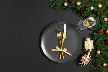 Fototapeta na wymiar Festive table setting with golden cutlery, gifts and fir branches on a black background. Preparing for Christmas dinner. Copy space, top view, flat lay.