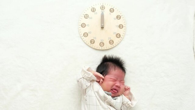 大泣きしてぐずっている産後1か月0歳の新生児の上に時計を配置した動画