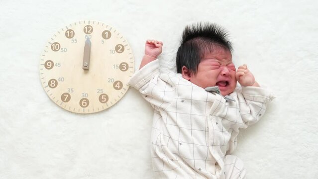 大泣きしてぐずっている産後1か月0歳の新生児の横に時計を配置した動画