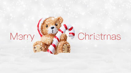 Merry Christmas text and teddy bear with red hat and candy striped cane stick isolated on snowing background, white Christmas concept template for greeting gift card or promotion advertising banner